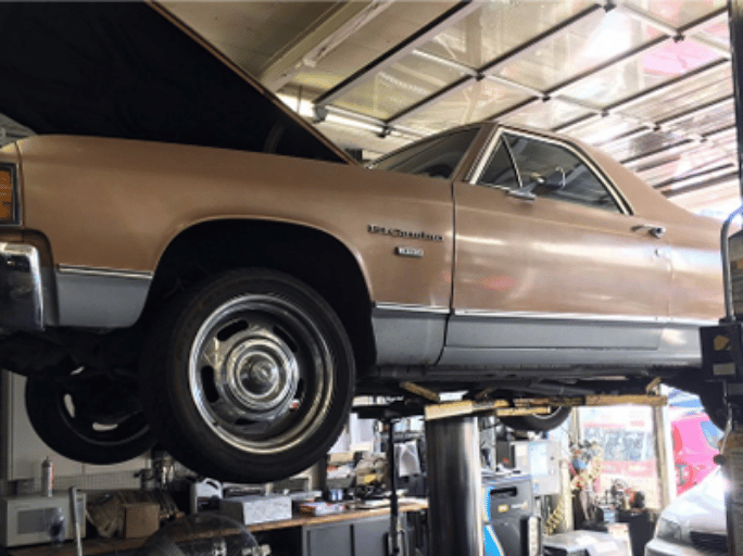 An El Camino is shown on a lift inside of the auto repair shop